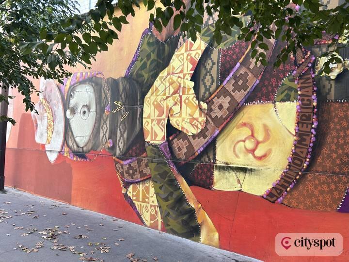 Inti's mural “Sudaka”: a patchwork-clad figure with a white mask, surrounded by Andean-style geometric patterns
