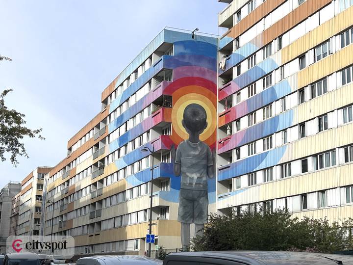 Seth's mural “Enter the Vortex”: a child seen from behind facing concentric rainbow circles painted across a tower block